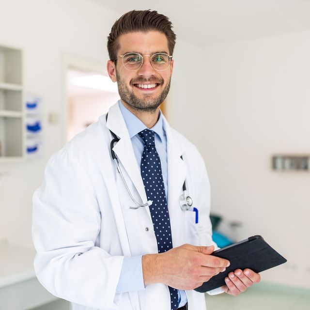 Doctor in white coat with stethoscope smiling in hospital corridor